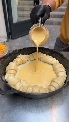 a person pouring batter on top of a pancake in a skillet with other food items