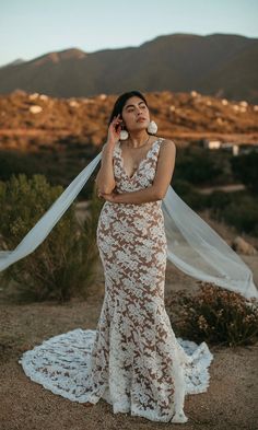 a woman standing in the desert wearing a wedding dress and holding a veil over her head