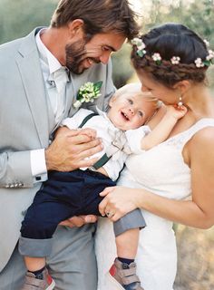 a man in a suit and tie holding a baby while standing next to a woman