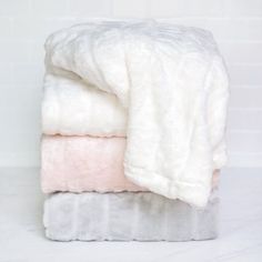 three blankets stacked on top of each other in white and light pink colors, against a white brick wall