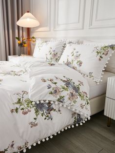 a white bed with flowers and pom poms on the pillowcase, next to a lamp