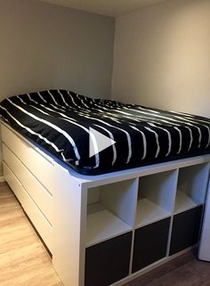 a bed with black and white sheets on top of it next to a book shelf