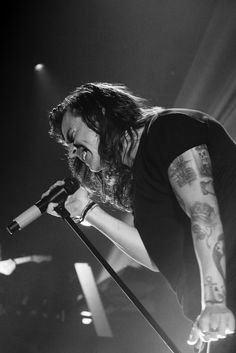 a man with long hair and tattoos on his arm holding a microphone in front of him