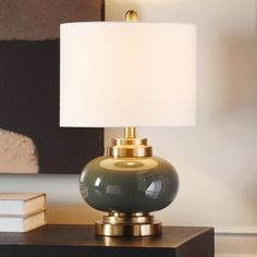 a table lamp sitting on top of a night stand next to a book and a painting