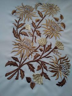 an embroidered piece with gold and brown flowers on white fabric, in the shape of leaves