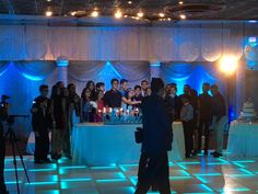 a group of people standing in front of a cake on a table with blue lights