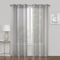 a white curtain hanging on the side of a window next to a table with a lamp