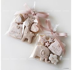 two decorated cookies in plastic bags on a white table with pink ribbon and bow around them