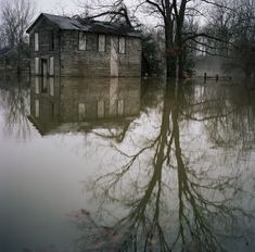 an old house is surrounded by water in the middle of a flooded area with trees