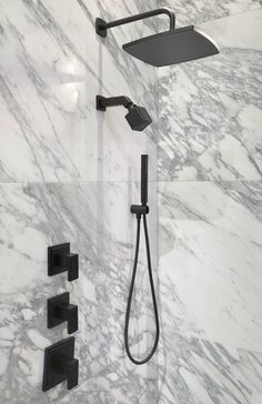 the shower head and handset are shown in this marble - like bathroom with black fixtures