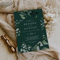 a green and white wedding card with greenery on the front, next to a bottle of wine