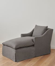 a gray chaise lounge chair sitting on top of a hard wood floor next to a white wall