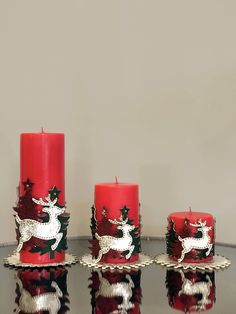 three red candles sitting on top of a table next to each other with christmas decorations