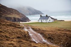 a house sitting on top of a lush green hillside next to the ocean with waves coming in