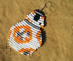 an orange and white beaded keychain on the sand with a star wars character