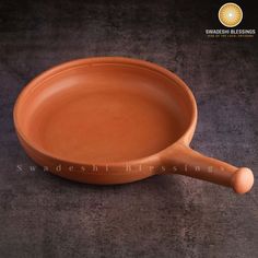 an orange pan with a wooden handle sitting on a gray surface in front of a black background