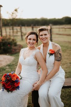 two brides sitting on a bench in front of a fence with flowers and greenery