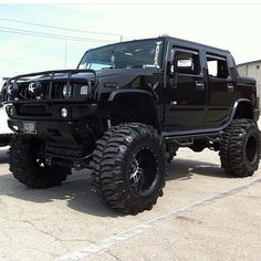 a black hummer truck parked in a parking lot next to a white wall and building