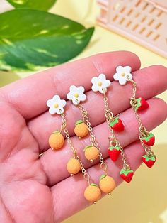 the small fruit charms are on display in someone's hand, with flowers and leaves hanging from them