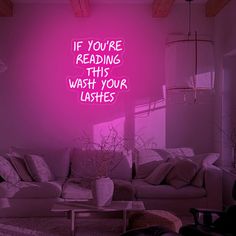 a living room filled with furniture and a neon sign above the couch that says if you're reading this wash your lashes