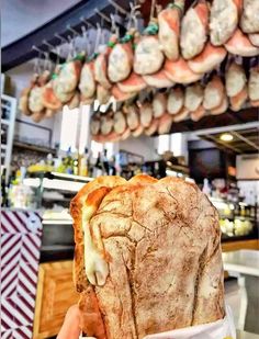 a person holding a piece of bread in front of some food hanging from the ceiling