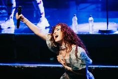 a woman with red hair holding a microphone in her right hand and singing on stage