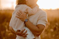 a man holding a woman in his arms while the sun goes down on him and she is wearing a watch