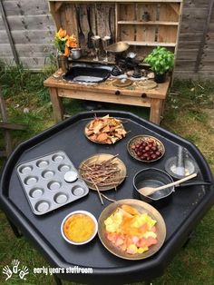 an outdoor table with many different foods on it and some utensils in bowls