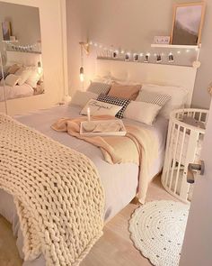 a white bed sitting in a bedroom next to a baby crib and mirror on the wall