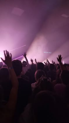 a crowd of people at a concert with their hands in the air and lights on