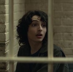 a man with curly hair standing in front of a brick wall