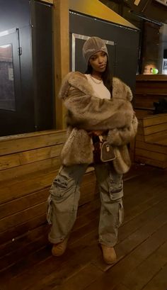 a woman standing on a wooden floor wearing a fur coat and hat with her hands in her pockets