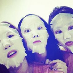 three women with facial masks on their faces posing for the camera, all wrapped in tissue paper