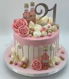 a pink cake with white frosting and flowers on top is decorated with champagne bottles