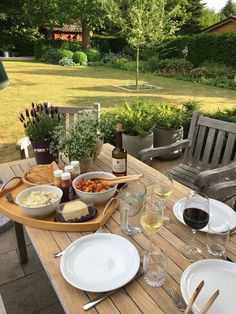 a wooden table topped with white plates and bowls filled with food next to wine glasses