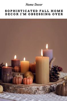 candles are arranged on a table with pine cones and pumpkins in the foreground text reads, home decor sophisticated fall home decor i'm obsesing over