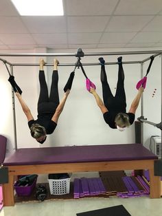 two people doing aerial acrobatic exercises in a pistah room with purple mats on the floor