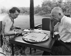 an old man and woman sitting at a table playing board games