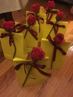 four yellow boxes with red roses tied to them on top of a wooden floor next to a person's feet