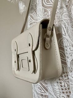 "It is a pre owned The Cambridge Satchel Company bag and shows signs of wear. The exterior does come with light scuffing at the edges and some surface scratches from normal used, no major flaws. The inside looks very clean and undamaged. The hardware is functional. This bag is in very good overall used condition. Bag length 6.5\" Bag height 5\" Bag depth 2\" Strap drop 26\"max. FREE DOMESTIC SHIPPING Please view the photos to evaluate the condition. Any questions regarding an item, ask prior to Classic Neutral Satchel Bag, Classic Beige Satchel With Detachable Strap, Vintage Cream Satchel For Travel, White Leather Bag With Hasp Closure, Classic Beige Crossbody Satchel, Classic White Leather Satchel, Classic Cream Rectangular Satchel, Vintage Cream Shoulder Bag With Detachable Strap, Vintage Cream Shoulder Bag With Adjustable Strap