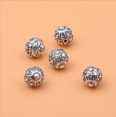 five silver beads with designs on them sitting on a pink surface in front of an orange background