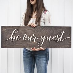 a woman holding a wooden sign that says be our guest on the front and back