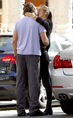 a man and woman kissing in front of parked cars on the side of the road