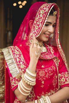 a woman in a red and gold bridal outfit is smiling at the camera while holding her hand to her ear