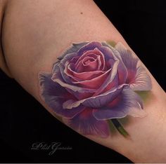 a pink rose tattoo on the left side of the arm, with purple petals and green leaves