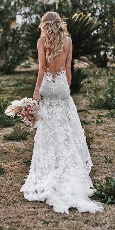 the back of a woman in a white wedding dress holding a bouquet and looking down