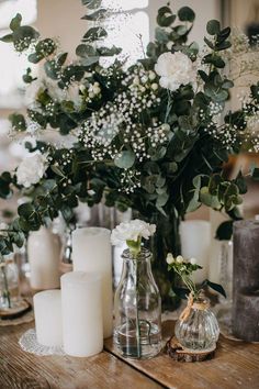 white flowers and greenery in glass vases on a wooden table with candle holders