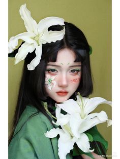 a girl with flowers painted on her face and hair is holding white lilies in front of her face