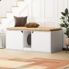 a white storage bench sitting under a stair case next to a potted plant and stairs