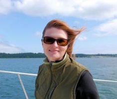 a woman on a boat in the water with her hair blowing back and sunglasses on